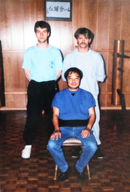 Michael - Philipp und Wong Drei Personen in einem Raum, zwei stehen hinter einer sitzenden Person.